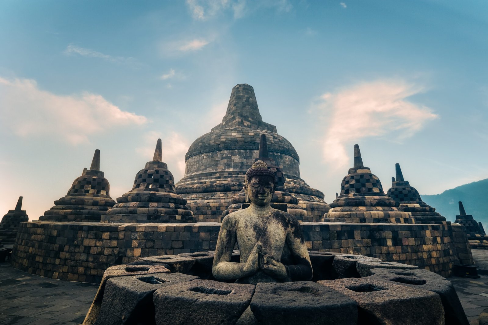 Amazing statue of meditating Buddha and stone stupas against blue sky on background. Ancient Borobudur Buddhist temple. Great religious architecture. Magelang, Central Java, Indonesia